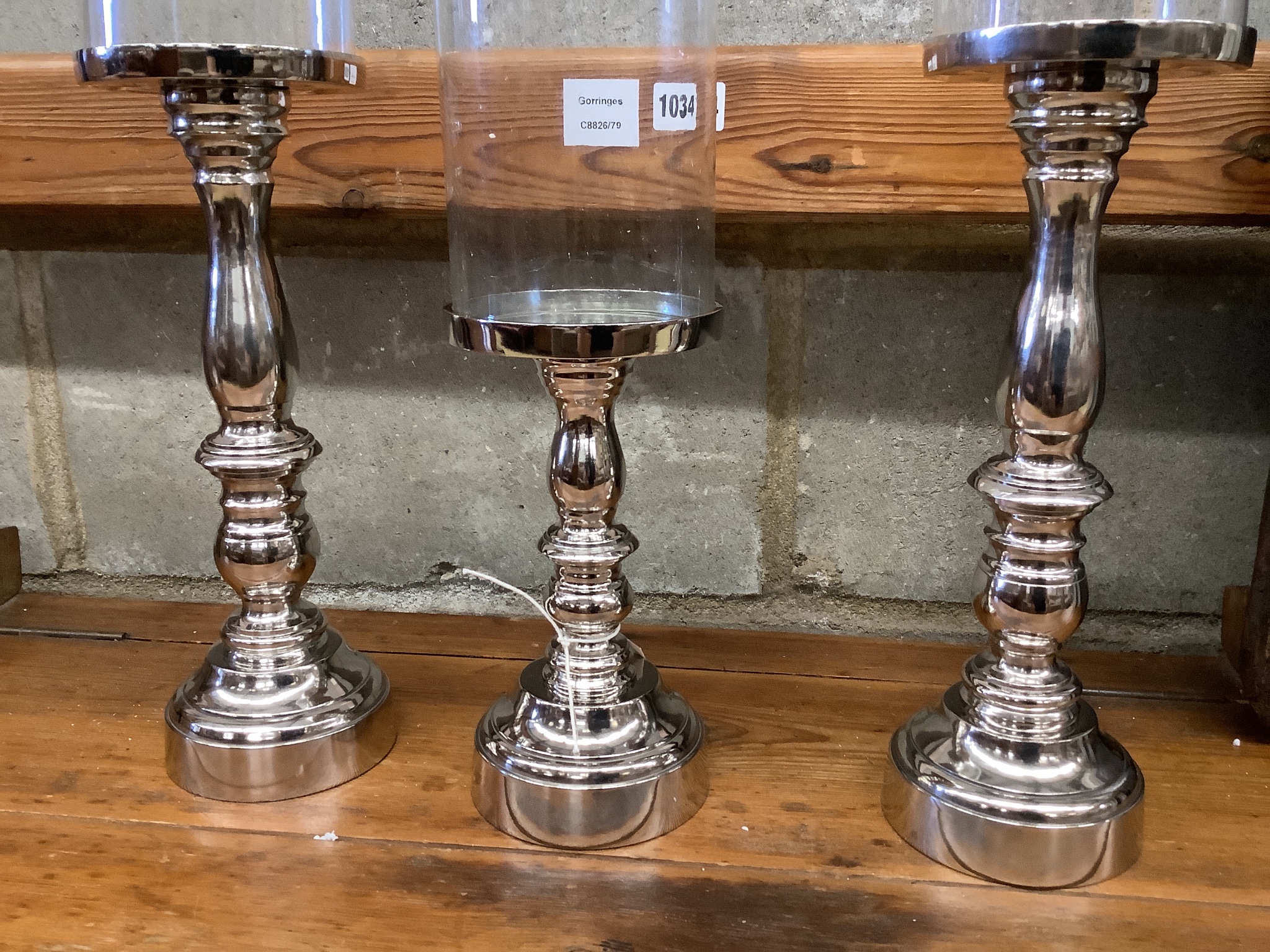 Set of three nickel plated candle stands with glass shades, height 51cm